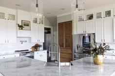 a kitchen with marble counter tops and white cabinets, gold vases on the island