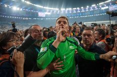 a man in a green shirt is surrounded by people at a soccer game with cameras around him