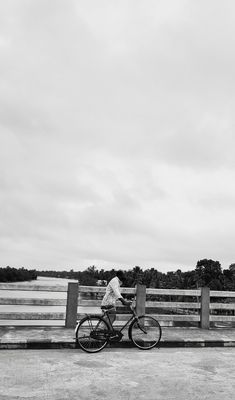 black and white photograph of a person riding a bike on the road near a wooden fence