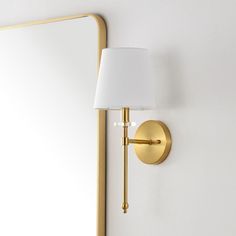 a wall light with a white shade on it and a mirror in front of it