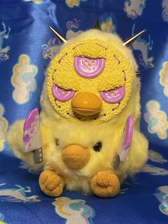 a yellow stuffed animal with pink and purple decorations on it's head sitting on a blue background