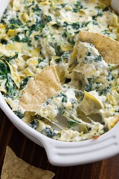 spinach and artichoke dip in a white casserole dish with tortilla chips