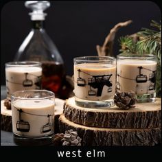 three candles sitting on top of a wooden table next to pine cones and an old fashioned decanter