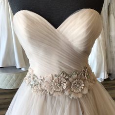 a wedding dress with flowers on the waist and belt is displayed in front of a mannequin