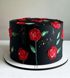 a black cake with red roses painted on the front and sides, sitting on a white plate