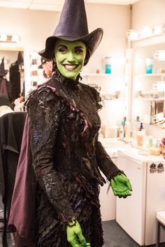 a man dressed up as a witch in a dressing room with green paint on his face and hands