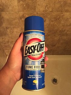 a person holding up a spray of easy - off cleaner in front of a bathtub