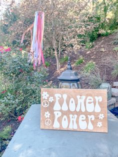 a wooden sign that says flower power on top of a cement table in front of some flowers