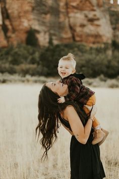 a woman holding a child in her arms while standing in a field with mountains in the background