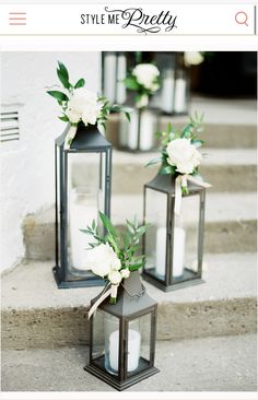 three black lanterns with white flowers and greenery sit on the steps next to each other