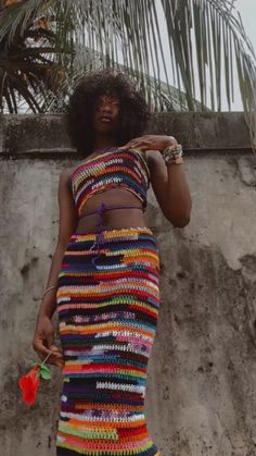 a woman standing in front of a palm tree wearing a multicolored knitted dress