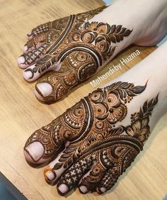 two feet with henna tattoos on them sitting on top of a wooden table next to each other