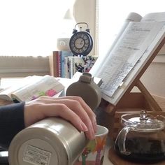 a person's hand on a coffee cup next to an open book and music sheet