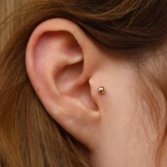 a woman's ear is shown with a tiny gold ball in the middle of it