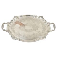 a silver tray with an oval handle and floral design on the bottom, holding two handles