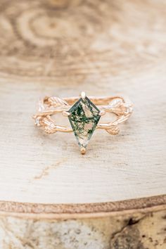 a gold ring with a green diamond on it sitting on top of a wooden table