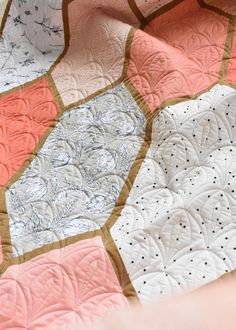 a close up of a quilt on a bed with pink and white colors, which has been made to look like hexagonal shapes