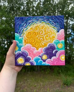 a hand holding up a colorful card with swirls and clouds in the sky on it