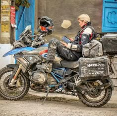 a woman is sitting on a motorcycle and looking at her cell phone in front of a building