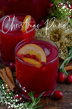 two glasses filled with cranberry punch and garnished with orange slices, cinnamon sticks, and christmas greenery