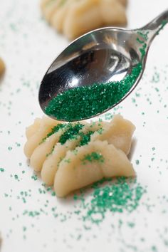 a spoon with green sprinkles on it and some cookies in the background