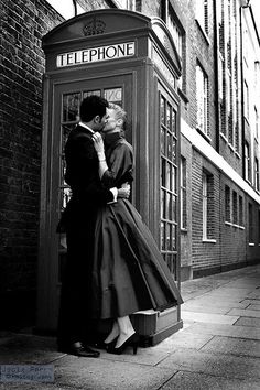 a man and woman kissing in front of a phone booth