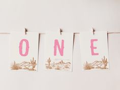 three cards hanging on a clothes line with the word one painted in pink and white