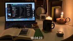 an open laptop computer sitting on top of a table next to a cup and candle