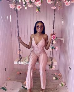 a woman sitting on a swing in a pink room with flowers hanging from the ceiling