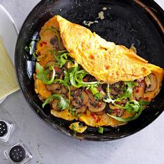 an omelet with mushrooms and greens in a skillet next to other dishes