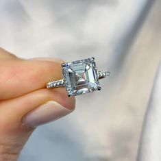 a close up of a person holding a ring with an emerald cut diamond in it