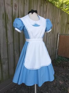 a blue and white dress on a mannequin head stand in front of a fence