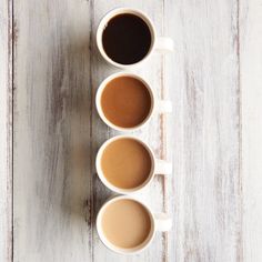 three cups of coffee sitting on top of a white wooden table next to each other