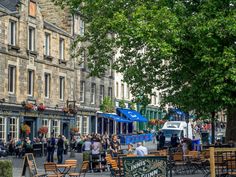 people are sitting at tables in the middle of an open city square with shops on both sides