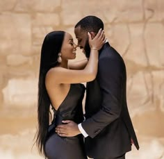 a man and woman embracing each other in front of a stone wall