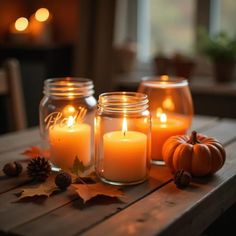 three mason jars filled with candles sitting on top of a wooden table next to autumn leaves