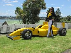 a woman standing next to a yellow race car on top of a lush green field