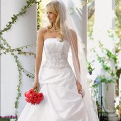 a woman in a white wedding dress holding a red bouquet and wearing a long veil