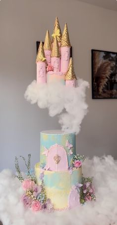 a three tiered cake with pink icing and gold crown on top, surrounded by fluffy clouds