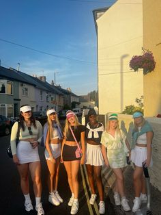 four young women in tennis outfits posing for a photo on the side of a road