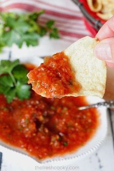 a hand holding up a piece of bread with sauce and parsley on the side