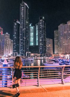 a woman is standing on a bridge looking at the water and buildings in the background