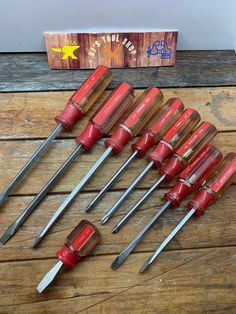 a set of seven red and silver tools on top of a wooden table next to a box