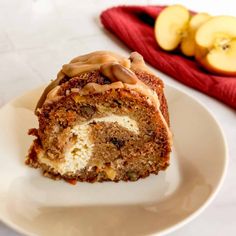 a piece of cake on a white plate with apples and nuts in the back ground