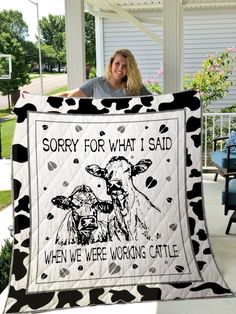 a woman holding up a black and white quilt with two cows on it that says sorry for what i said when we're working cattle