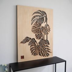 a wooden wall hanging on the side of a white wall next to a black shelf