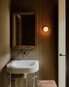 a white sink sitting under a bathroom mirror next to a wooden wall mounted light fixture