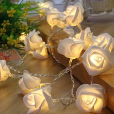 some white roses are sitting on a table with string lights around them and flowers in the background