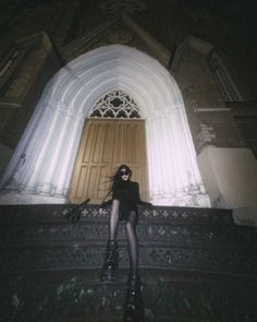 a woman is sitting on the steps in front of a church door with her legs crossed