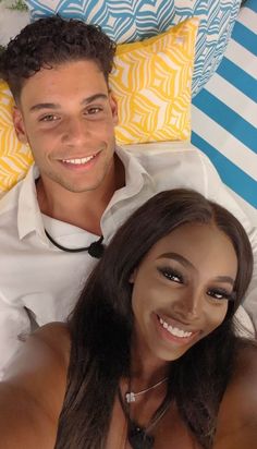 a man and woman laying on top of a bed next to each other smiling at the camera